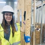 Mary in safety gear next to a construction frame.